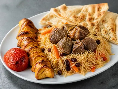 Representative Afghan qabuli rice with lamb chunks, chicken kabob, carrots, raisins, roasted tomato, and naan selected for Afghan Kabob Restaurant