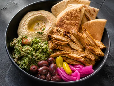 Representative a chicken shawarma pita platter with hummus, tabbouleh, olives, and warm flatbread selected for Omar's Pitas & Platters